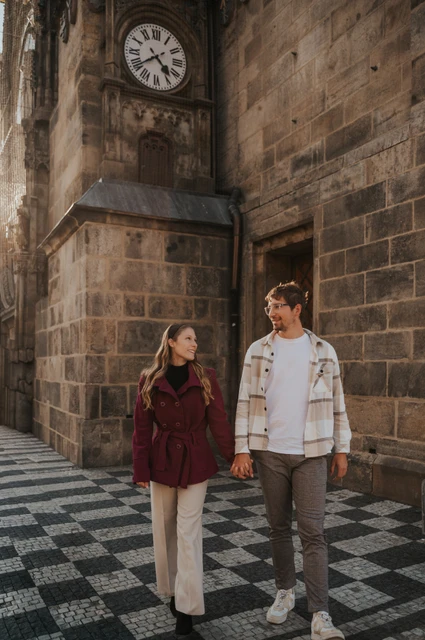 Prague couple photoshoot: couple walking hand in hand beneath the clock. Couple walking hand in hand beneath the clock during a couple photoshoot in Prague.