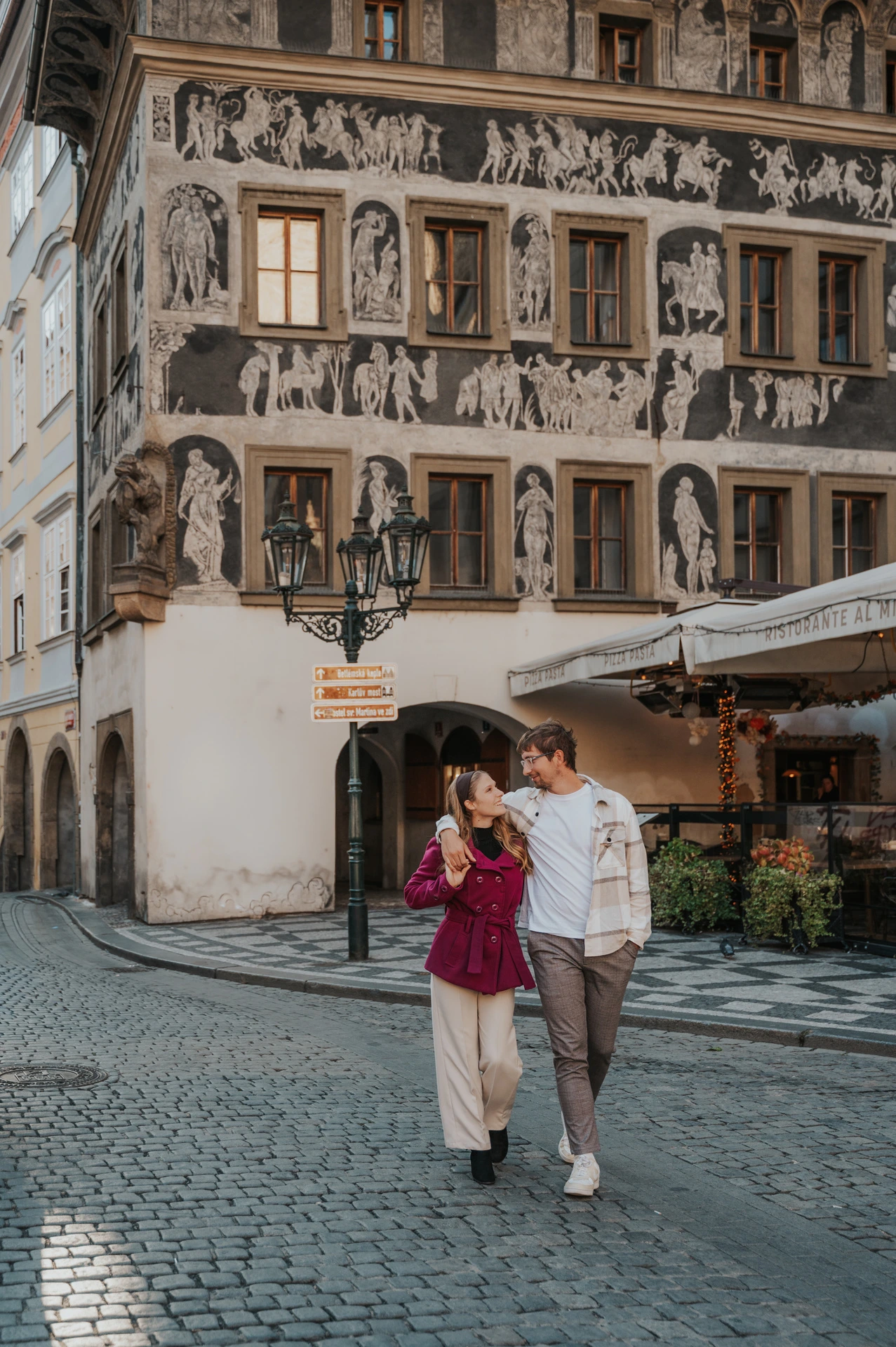 Couple walking towards the camera beside the decorated building during a couple photoshoot in Prague.
