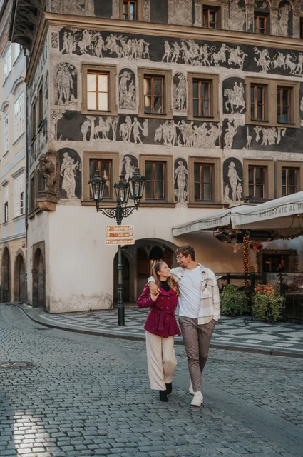 Prague couple photoshoot: couple walking towards the camera beside the decorated building. Couple walking towards the camera beside the decorated building during a couple photoshoot in Prague.