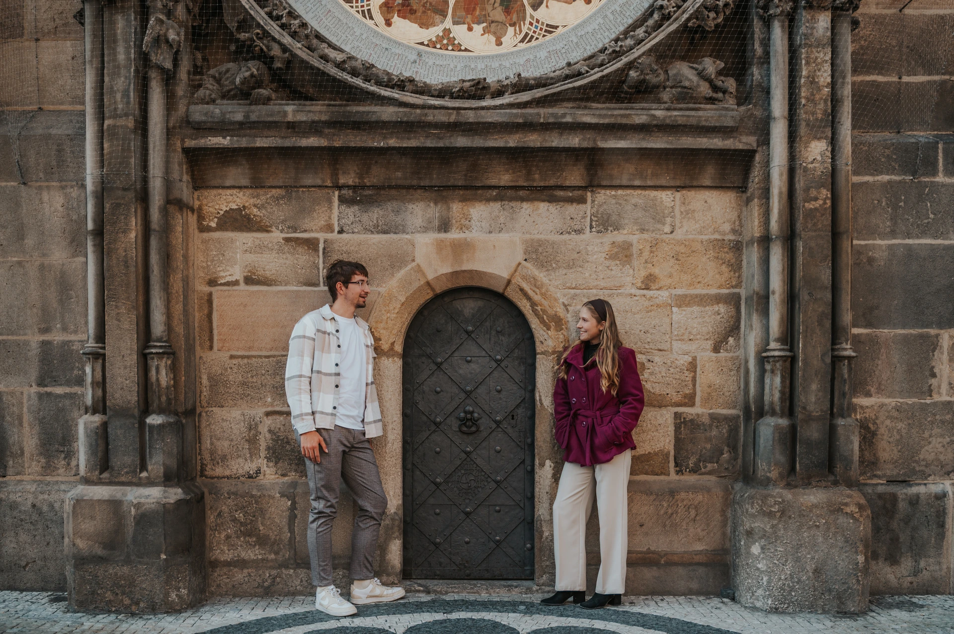 Prague couple photoshoot: wide portrait below the Astronomical Clock face. Wide portrait below the Astronomical Clock face during a couple photoshoot in Prague.