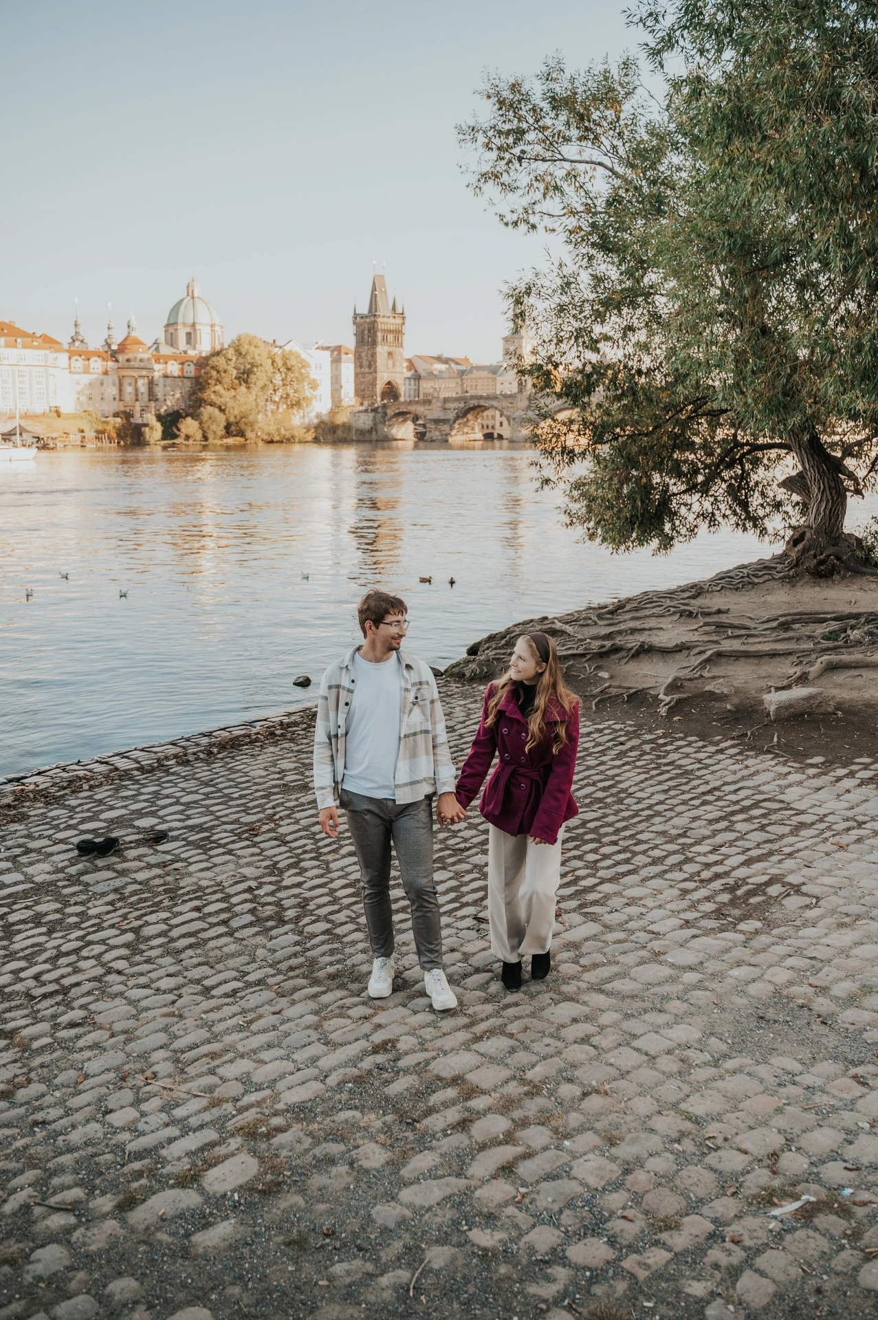 Wide view of the couple walking along the riverbank during a couple photoshoot in Prague.