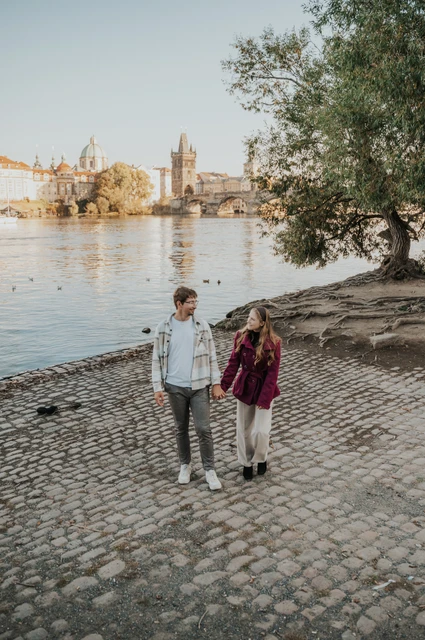 Prague couple photoshoot: wide view of the couple walking along the riverbank. Wide view of the couple walking along the riverbank during a couple photoshoot in Prague.