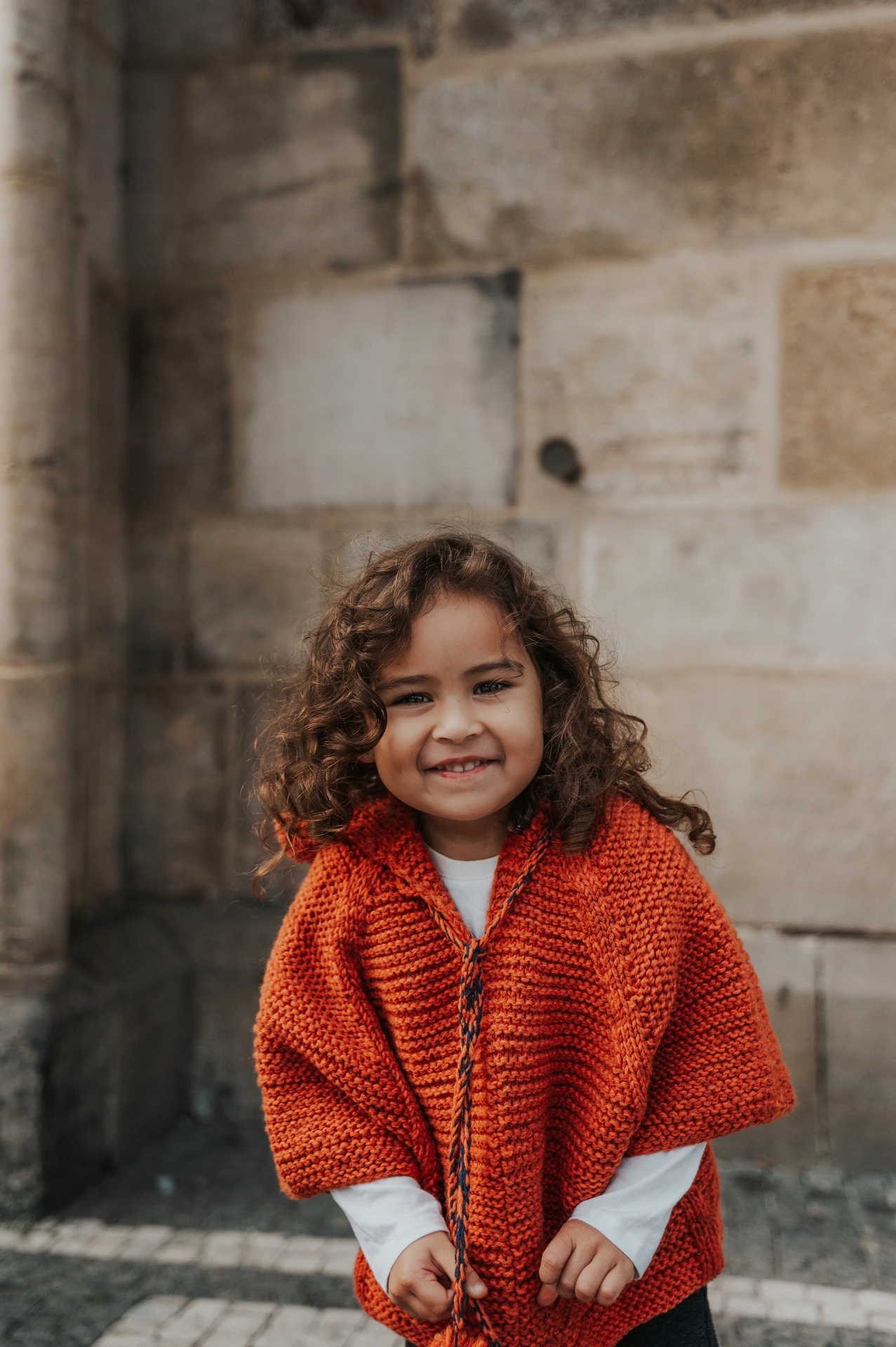 Little girl leaning forward with a playful smile during a mother and daughter family photoshoot in Prague.