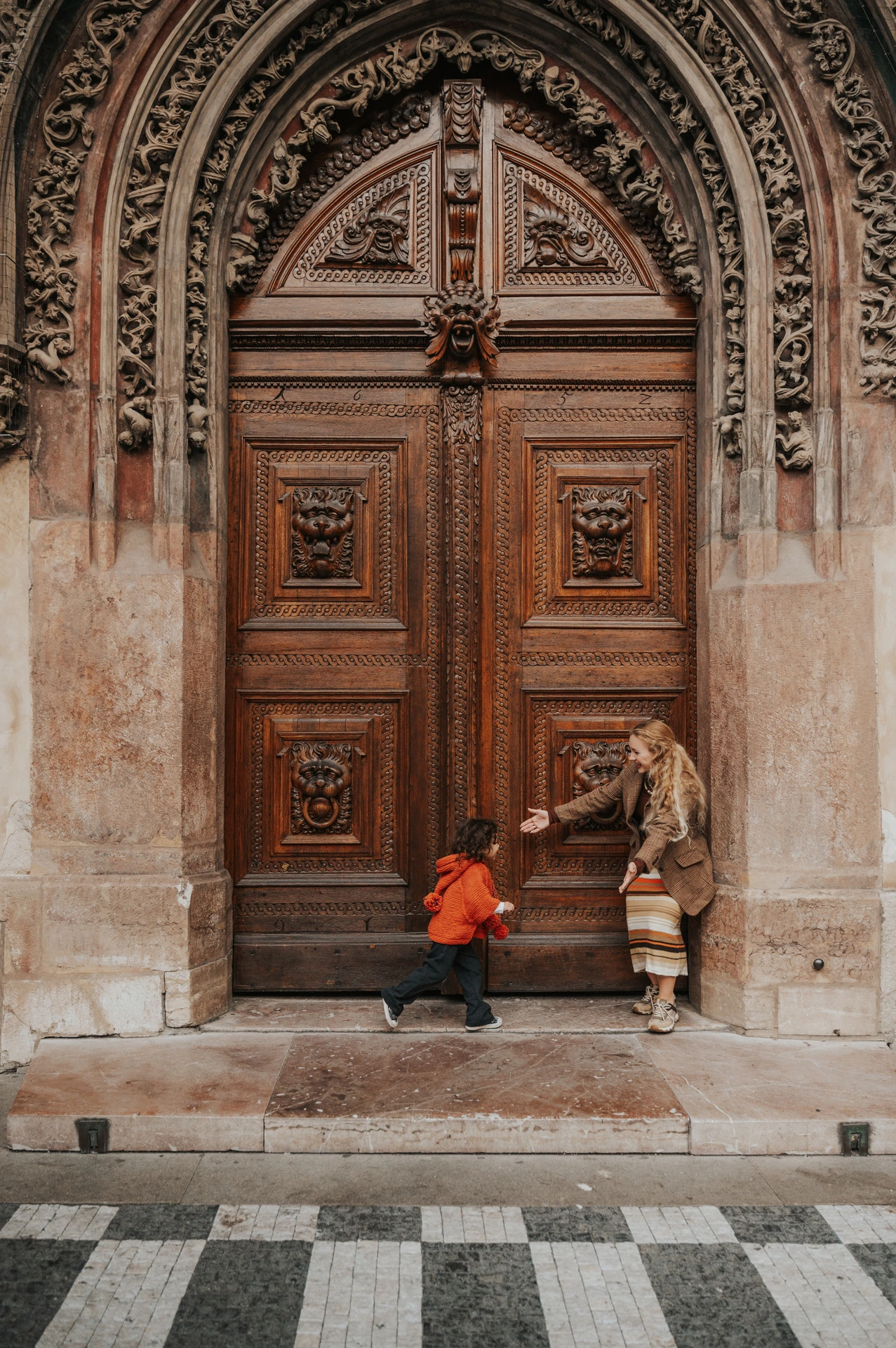 Little girl playing beside her mother at the wooden entrance during a mother and daughter family photoshoot in Prague.