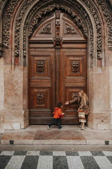 Prague family photoshoot: little girl playing beside her mother at the wooden entrance. Little girl playing beside her mother at the wooden entrance during a mother and daughter family photoshoot in Prague.