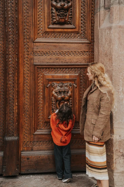 Prague family photoshoot: little girl reaching towards the carved wooden door beside her mother. Little girl reaching towards the carved wooden door beside her mother during a mother and daughter family photoshoot in Prague.