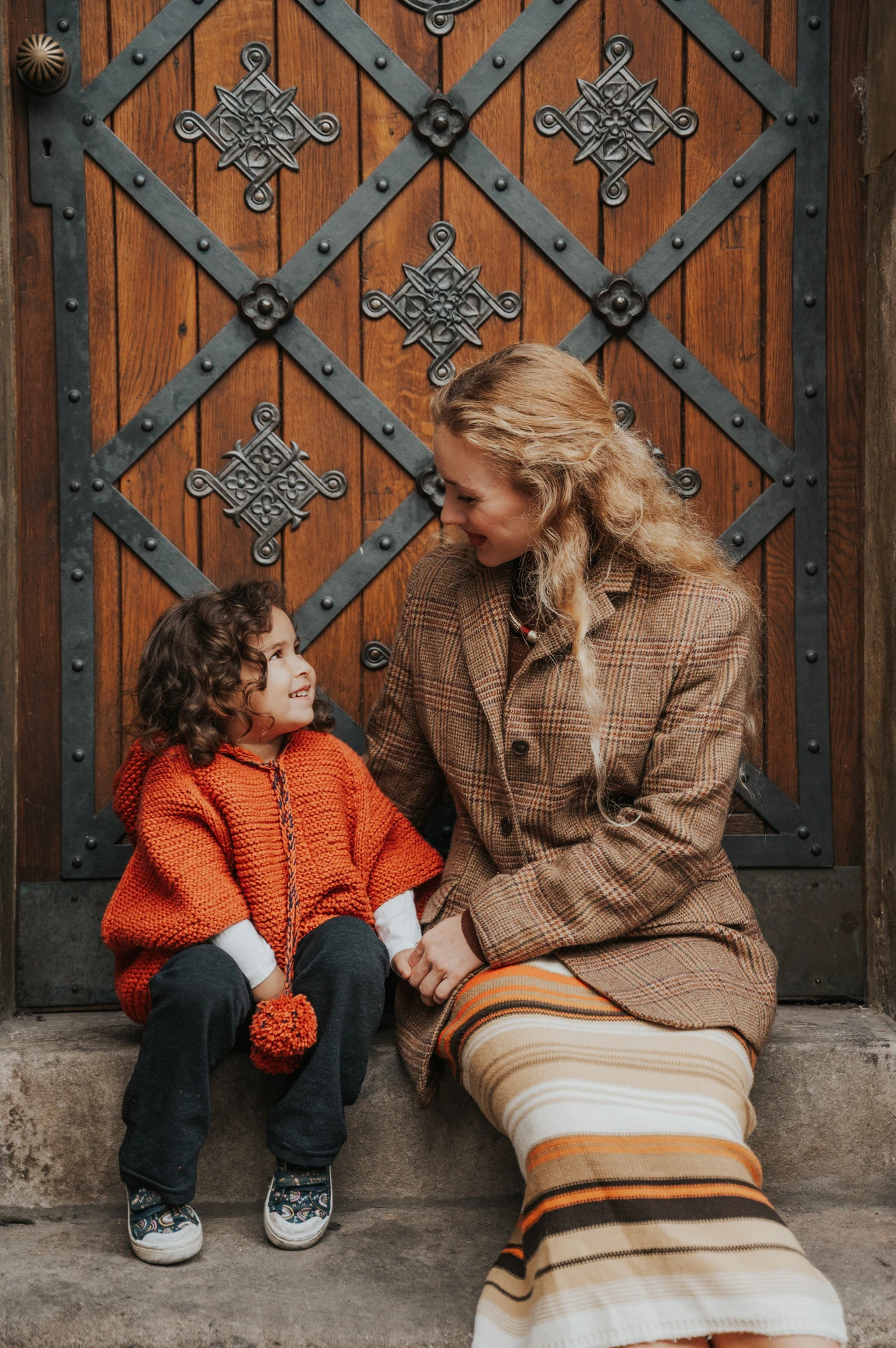 Mother and daughter smiling at each other on the doorstep during a mother and daughter family photoshoot in Prague.