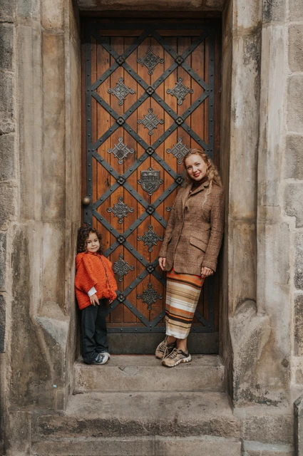 Prague family photoshoot: mother and daughter standing beneath a decorated wooden door. Mother and daughter standing beneath a decorated wooden door during a mother and daughter family photoshoot in Prague.