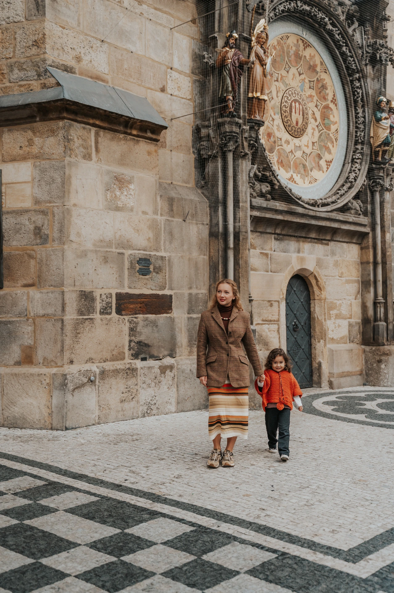Mother and daughter standing hand in hand beneath the clock during a mother and daughter family photoshoot in Prague.