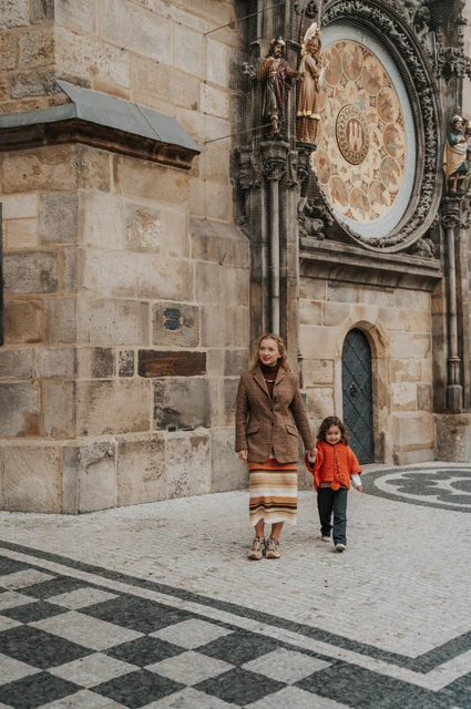 Prague family photoshoot: mother and daughter standing hand in hand beneath the clock. Mother and daughter standing hand in hand beneath the clock during a mother and daughter family photoshoot in Prague.