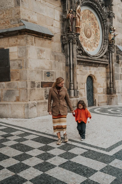 Prague family photoshoot: mother and daughter walking across the patterned pavement. Mother and daughter walking across the patterned pavement during a mother and daughter family photoshoot in Prague.