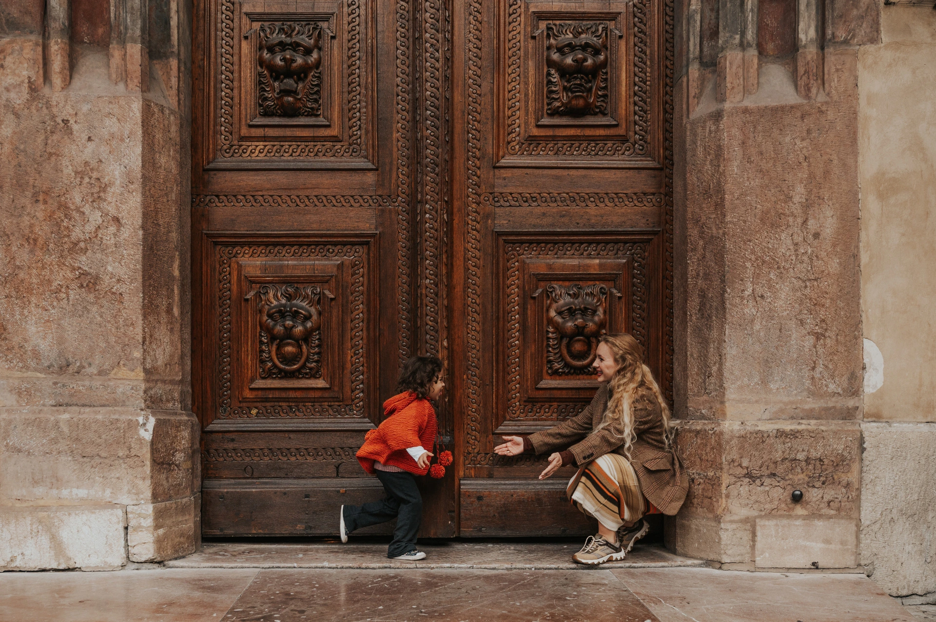 Mother crouching beside her daughter in front of the carved doors during a mother and daughter family photoshoot in Prague.