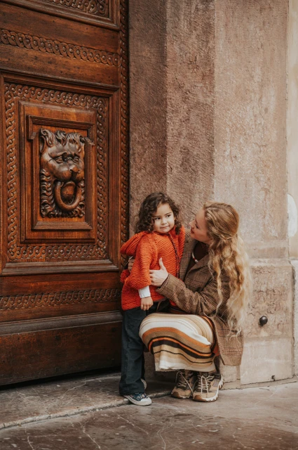 Prague family photoshoot: mother crouching for a kiss beside the carved door. Mother crouching for a kiss beside the carved door during a mother and daughter family photoshoot in Prague.