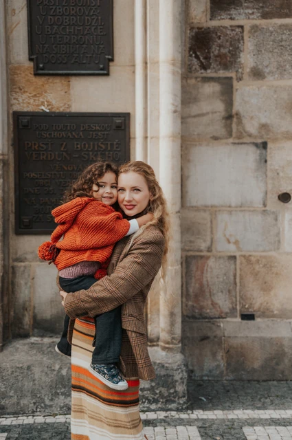 Prague family photoshoot: mother cuddling her daughter beside the Old Town wall. Mother cuddling her daughter beside the Old Town wall during a mother and daughter family photoshoot in Prague.