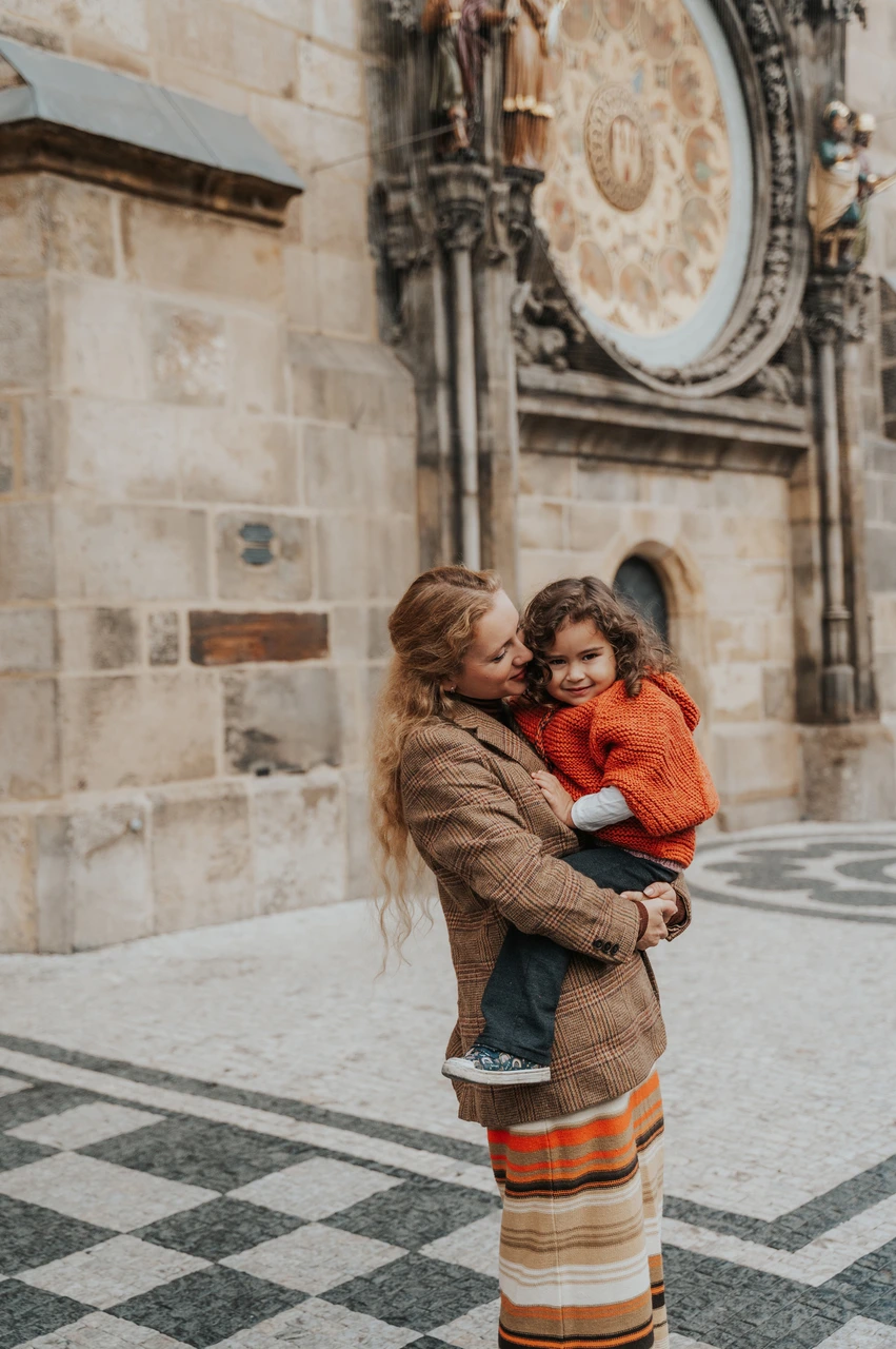 Prague family photoshoot: mother kissing her daughter beside the clock tower wall. Mother kissing her daughter beside the clock tower wall during a mother and daughter family photoshoot in Prague.