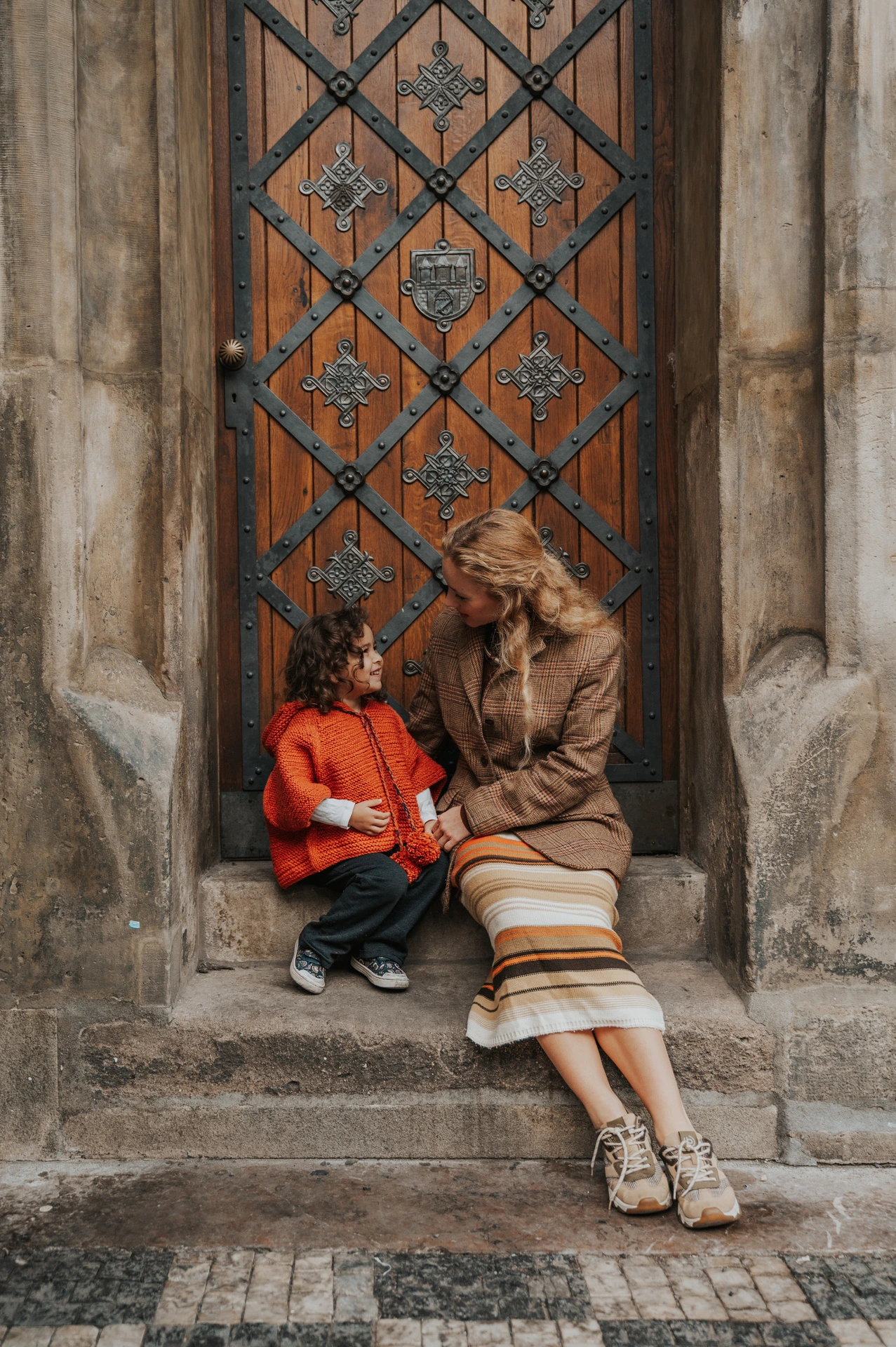 Mother sitting beside her daughter in the Old Town doorway during a mother and daughter family photoshoot in Prague.