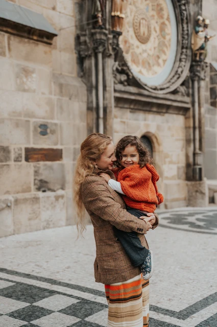 Prague family photoshoot: mother smiling while holding her daughter near the clock. Mother smiling while holding her daughter near the clock during a mother and daughter family photoshoot in Prague.