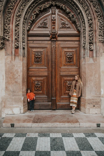 Prague family photoshoot: wide portrait of mother and daughter at an ornate Old Town entrance. Wide portrait of mother and daughter at an ornate Old Town entrance during a mother and daughter family photoshoot in Prague.