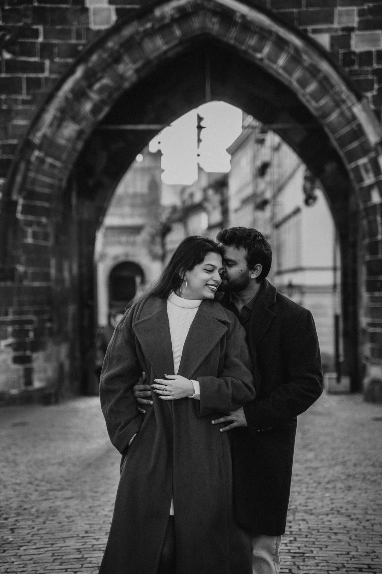 Black and white embrace beneath the Gothic arch during a couple photoshoot in Prague.