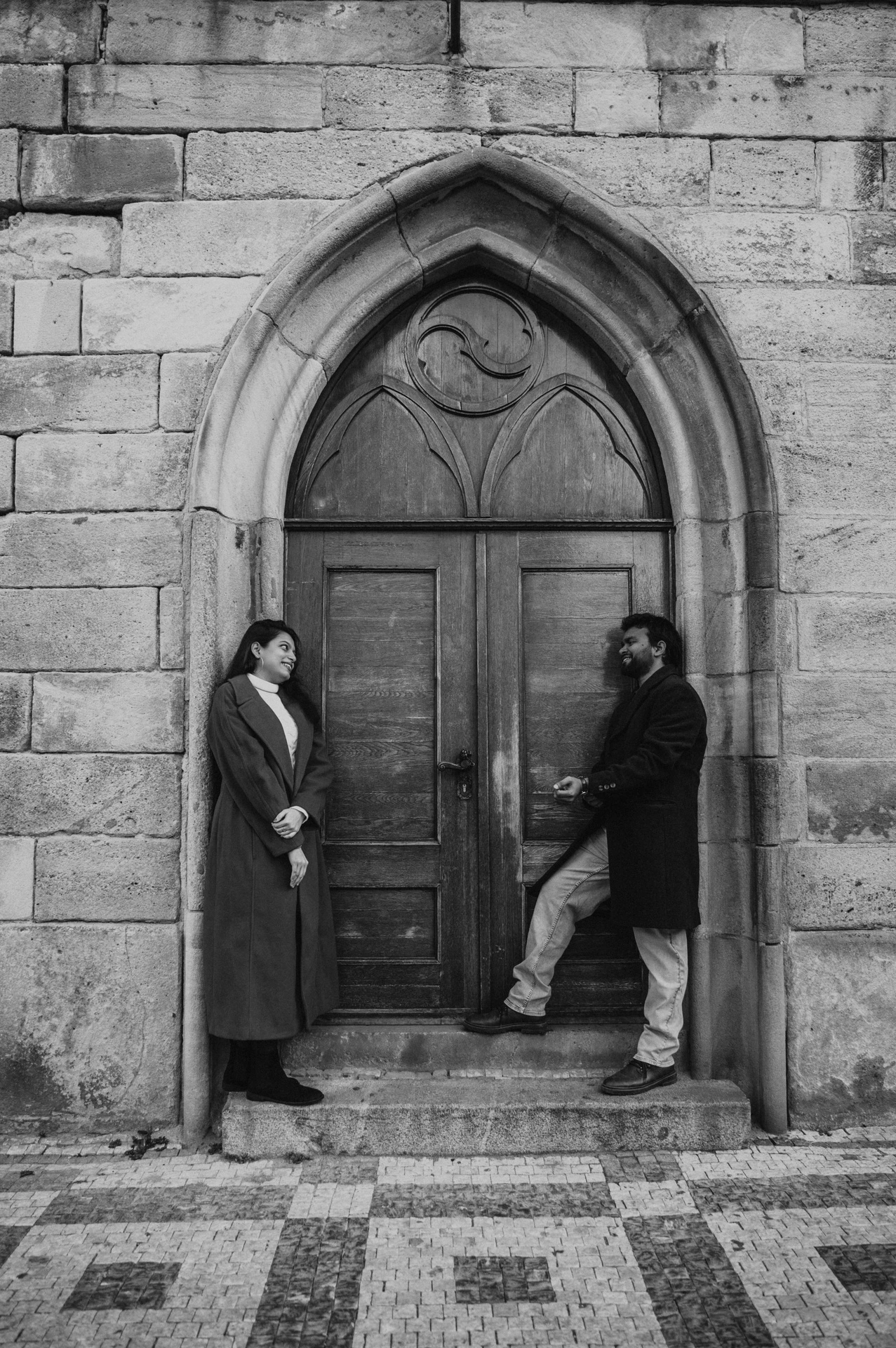 Black and white portrait at the arched wooden door during a couple photoshoot in Prague.