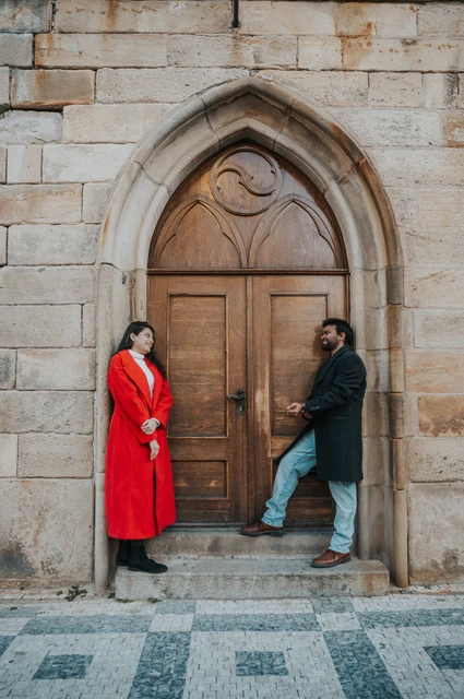 Prague couple photoshoot: couple facing each other beside an arched wooden door. Couple facing each other beside an arched wooden door during a couple photoshoot in Prague.