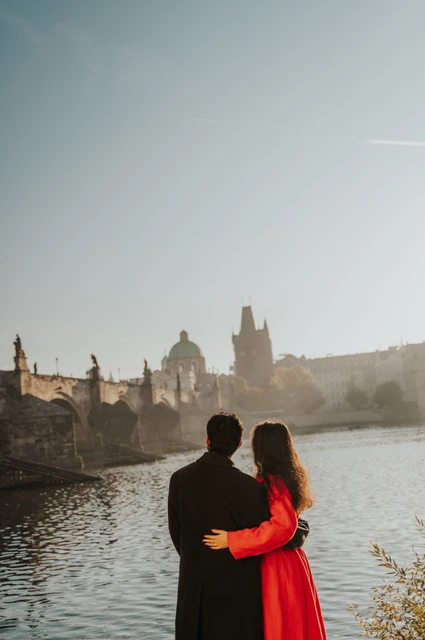 Prague couple photoshoot: couple holding each other beside the sunlit river. Couple holding each other beside the sunlit river during a couple photoshoot in Prague.