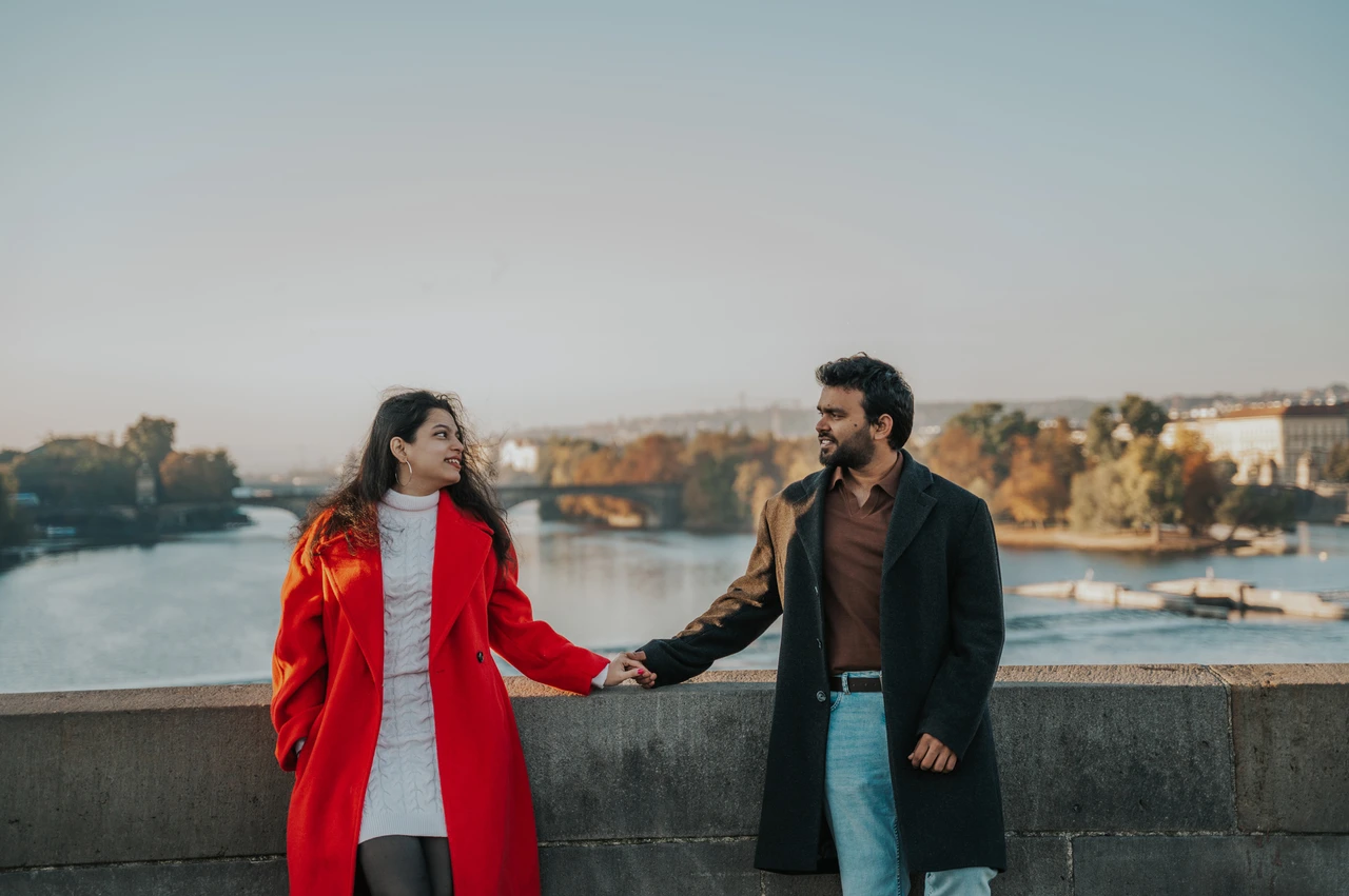 Prague couple photoshoot: couple holding hands with the river behind them. Couple holding hands with the river behind them during a couple photoshoot in Prague.