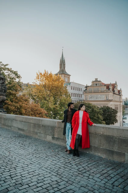 Prague couple photoshoot: couple leaning together beside autumn trees on Charles Bridge. Couple leaning together beside autumn trees on Charles Bridge during a couple photoshoot in Prague.