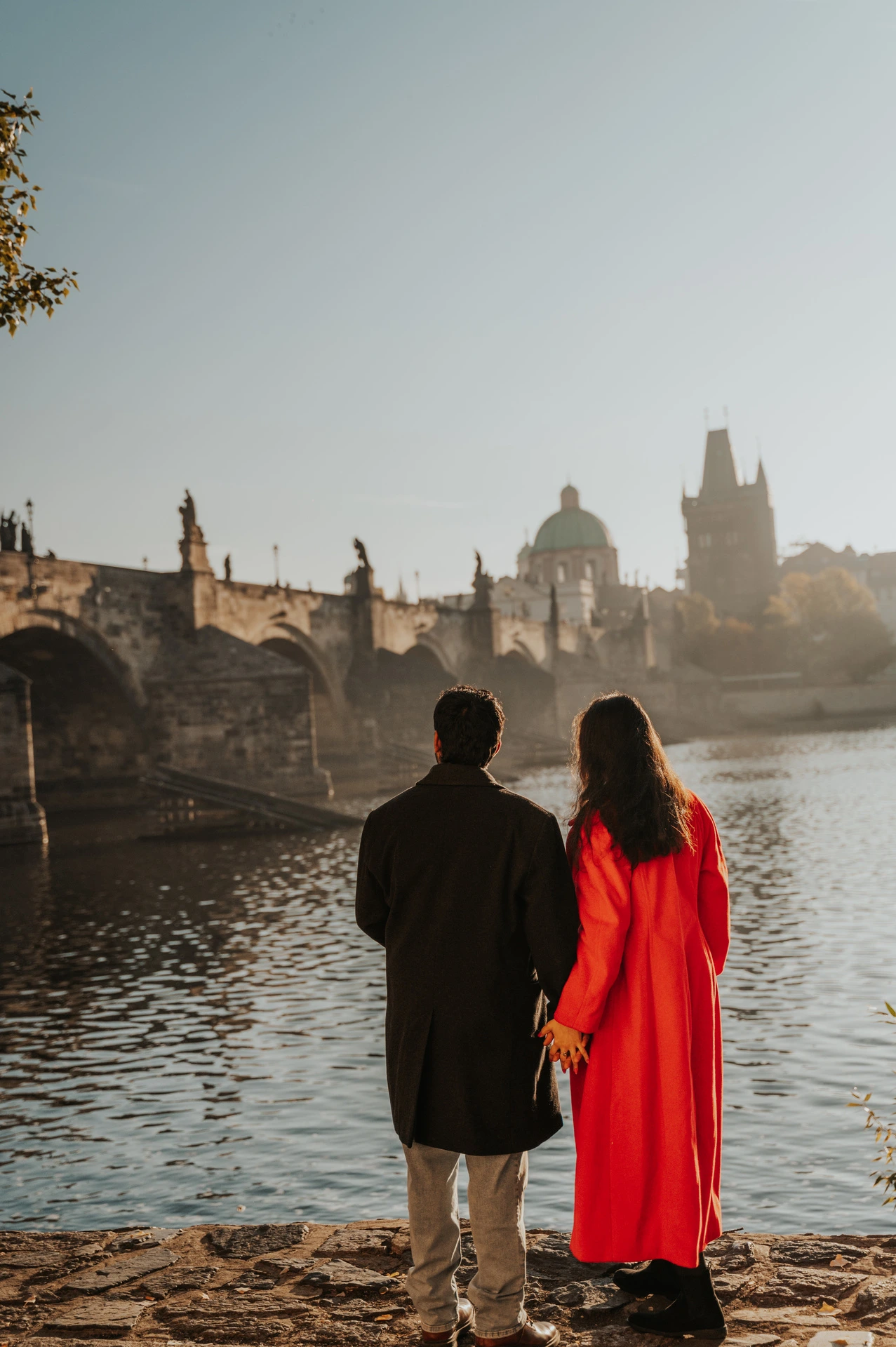 Couple looking across the Vltava towards the bridge during a couple photoshoot in Prague.