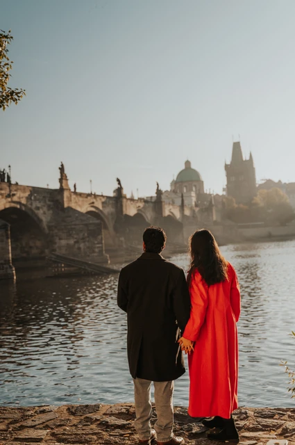 Prague couple photoshoot: couple looking across the Vltava towards the bridge. Couple looking across the Vltava towards the bridge during a couple photoshoot in Prague.