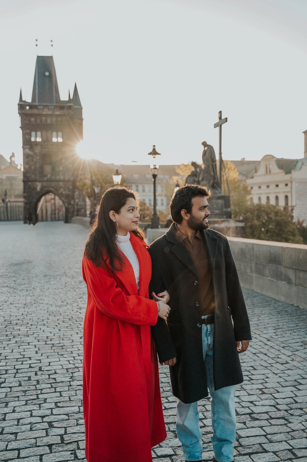 Couple walking side by side towards the bridge tower during a couple photoshoot in Prague.