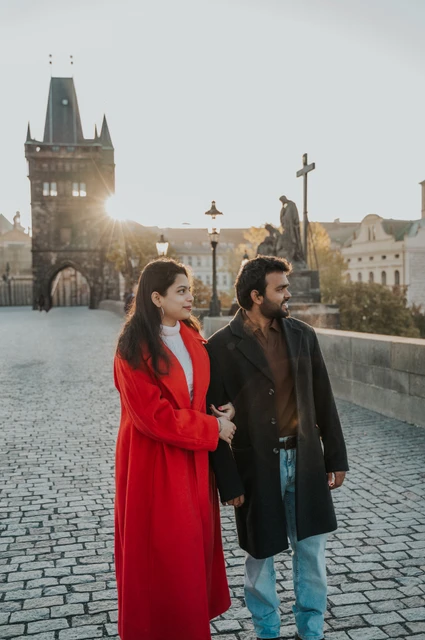 Prague couple photoshoot: couple walking side by side towards the bridge tower. Couple walking side by side towards the bridge tower during a couple photoshoot in Prague.