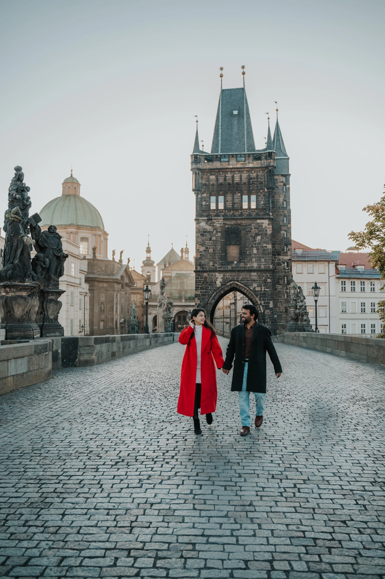 Couple walking towards the Old Town tower on Charles Bridge during a couple photoshoot in Prague.