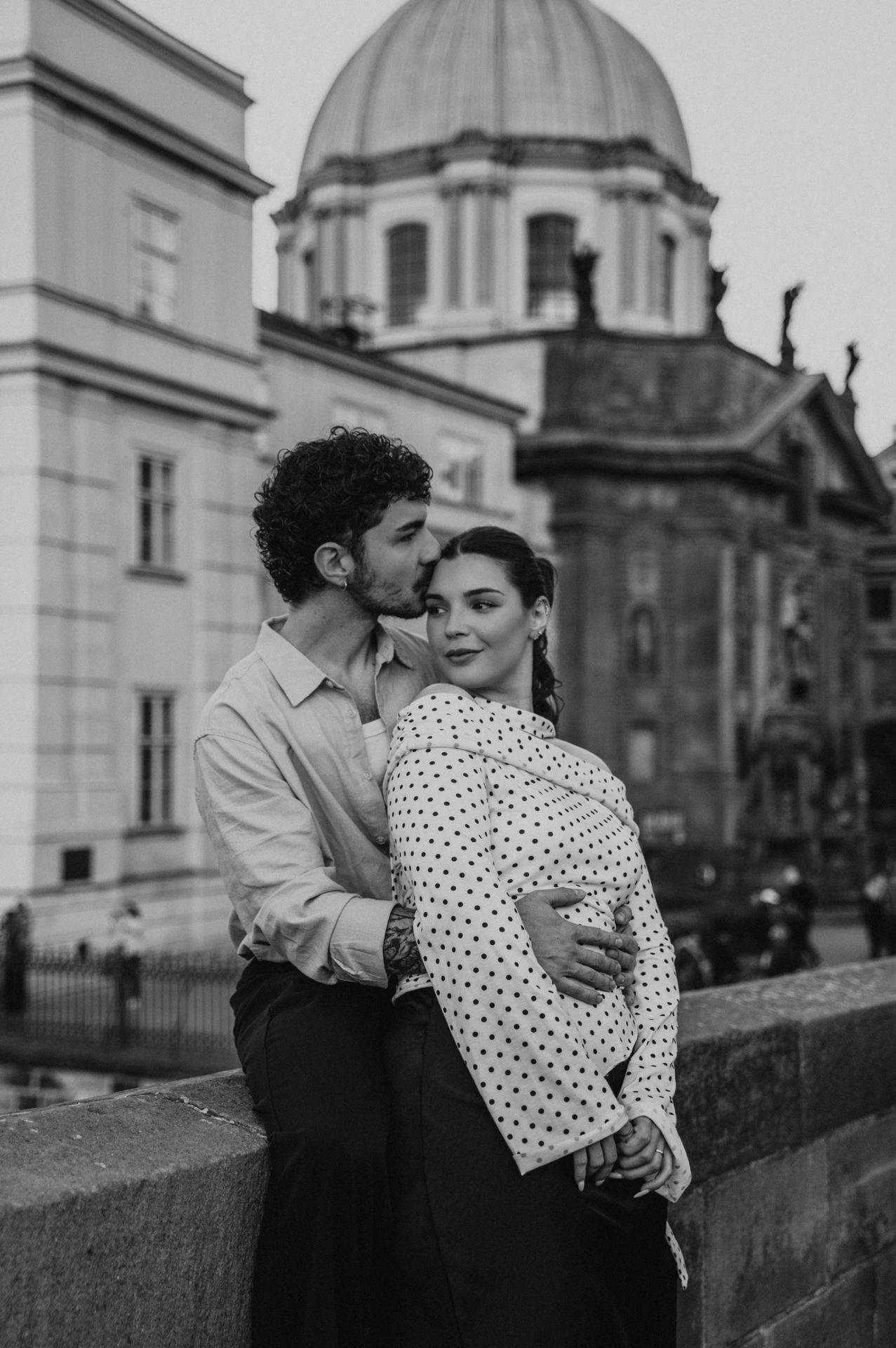 Black and white embrace with the green dome behind them during a couple photoshoot in Prague.