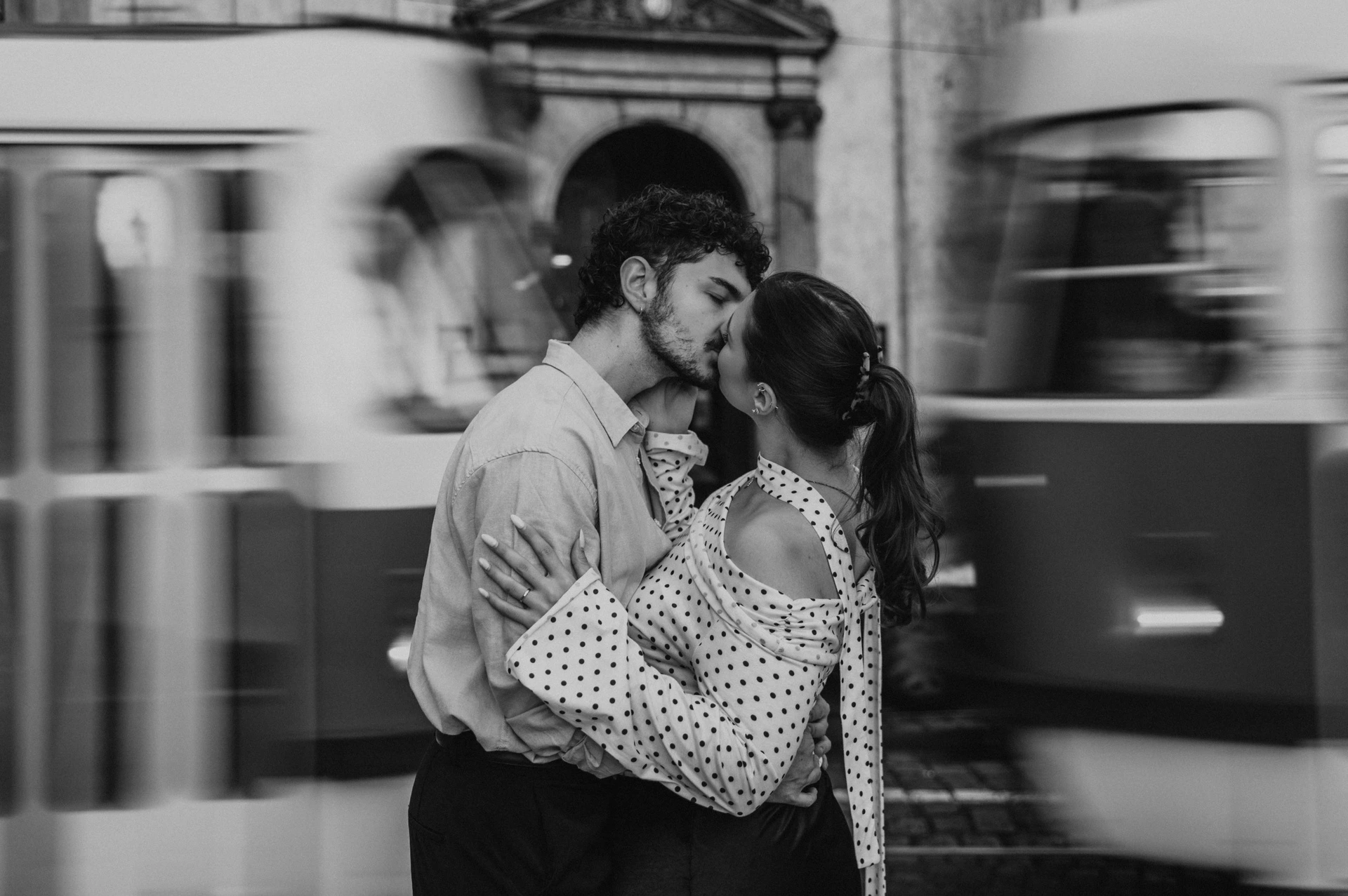Black and white kiss with a tram passing behind during a couple photoshoot in Prague.