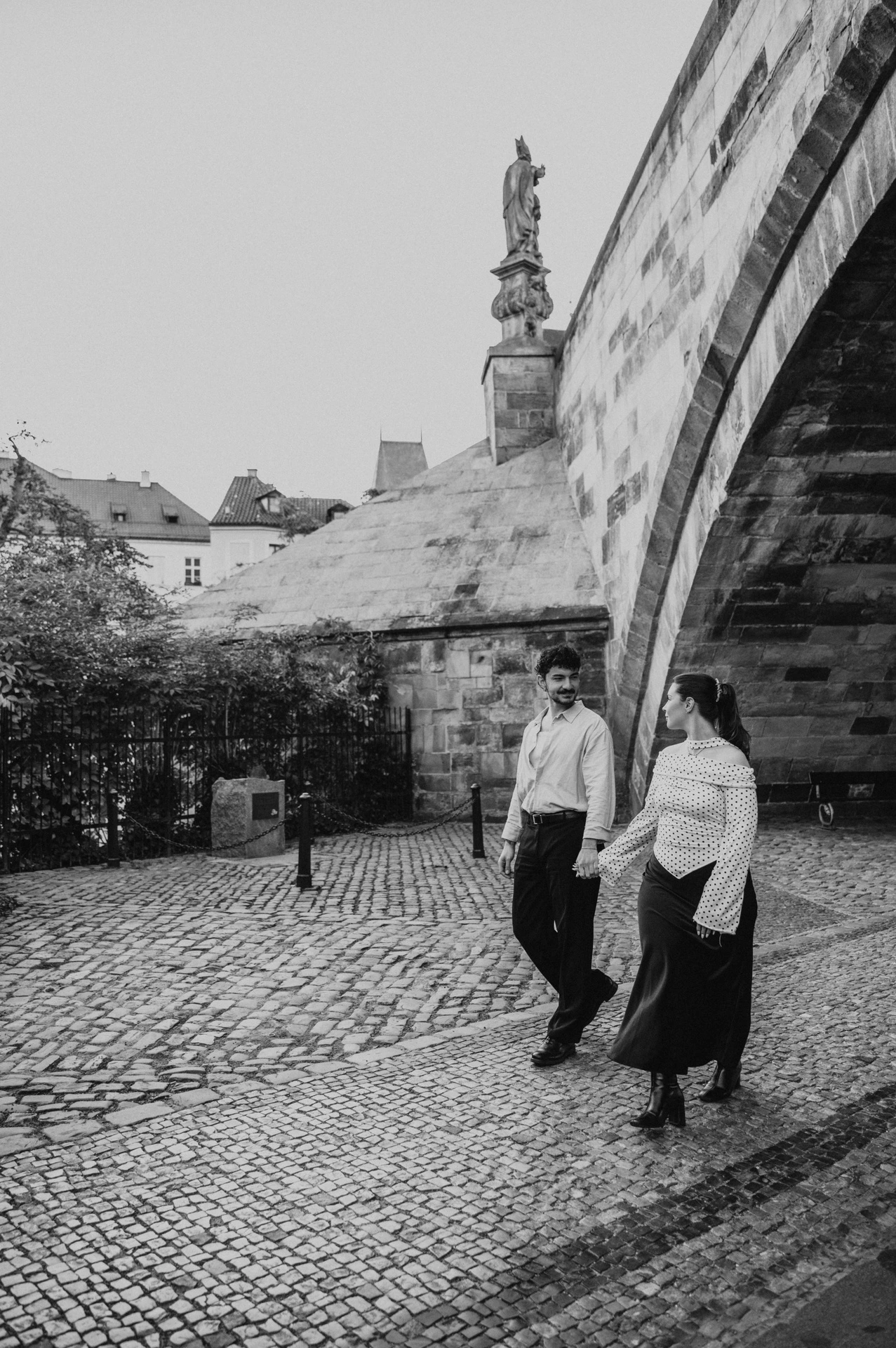 Black and white portrait beneath the Charles Bridge arch during a couple photoshoot in Prague.