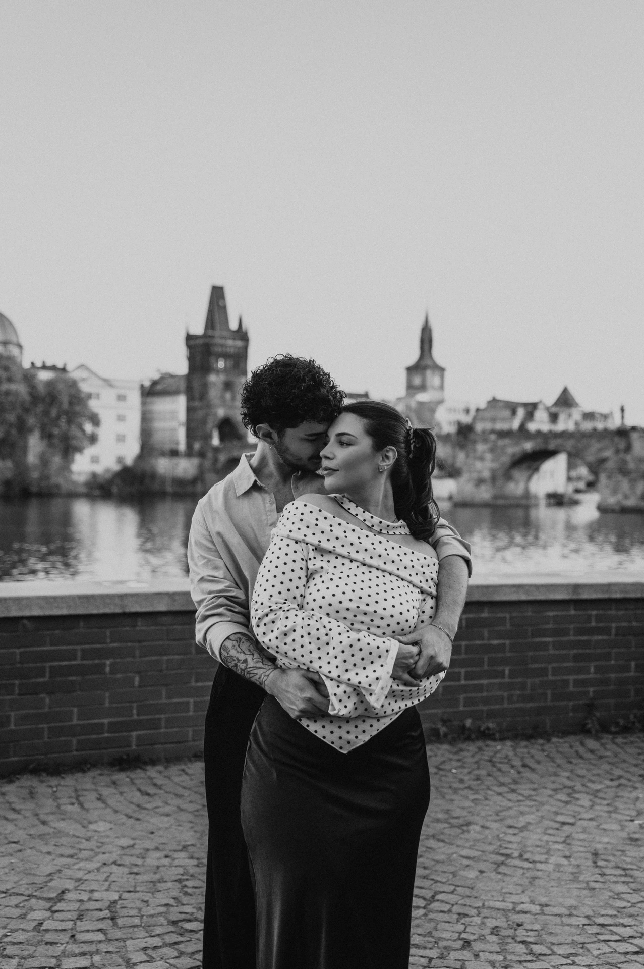 Black and white portrait of a close embrace by the Vltava during a couple photoshoot in Prague.