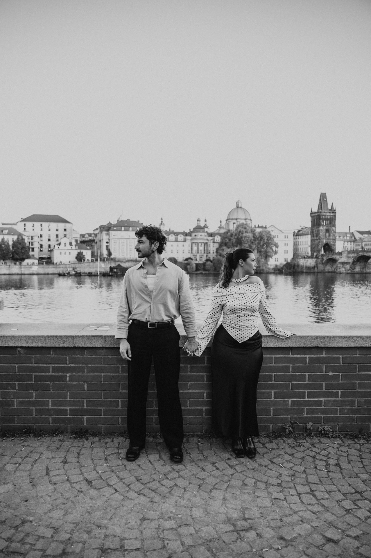 Black and white portrait of the couple by the brick river wall during a couple photoshoot in Prague.