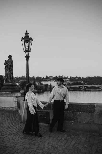 Prague couple photoshoot: black and white portrait of the couple holding hands on the bridge. Black and white portrait of the couple holding hands on the bridge during a couple photoshoot in Prague.