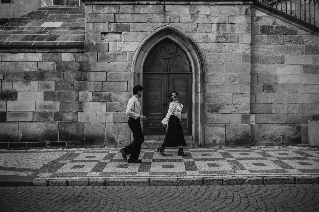 Prague couple photoshoot: black and white walk past the arched wooden doorway. Black and white walk past the arched wooden doorway during a couple photoshoot in Prague.
