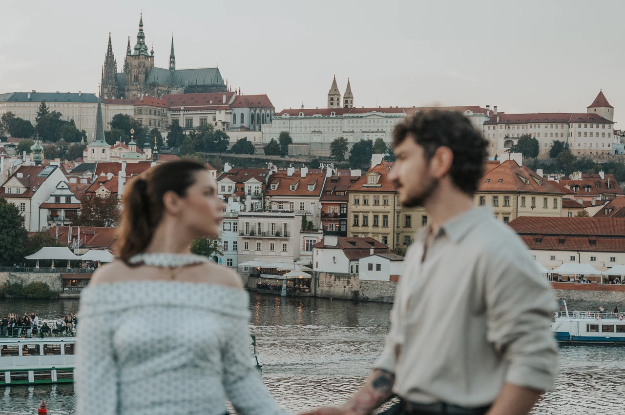 Prague couple photoshoot: close portrait of the couple with Prague Castle across the water. Close portrait of the couple with Prague Castle across the water during a couple photoshoot in Prague.
