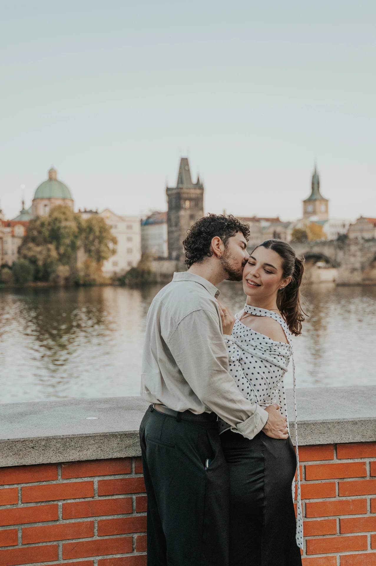 Couple cuddling with the Charles Bridge towers behind them during a couple photoshoot in Prague.