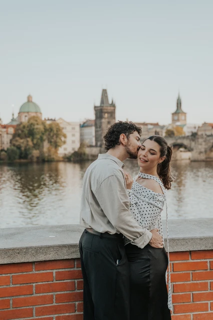 Prague couple photoshoot: couple cuddling with the Charles Bridge towers behind them. Couple cuddling with the Charles Bridge towers behind them during a couple photoshoot in Prague.