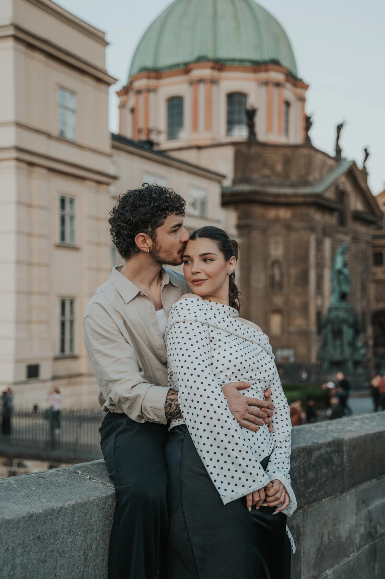 Couple embracing below a green dome beside Charles Bridge during a couple photoshoot in Prague.