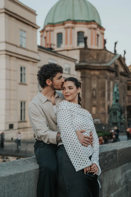 Couple embracing below a green dome beside Charles Bridge during a couple photoshoot in Prague.