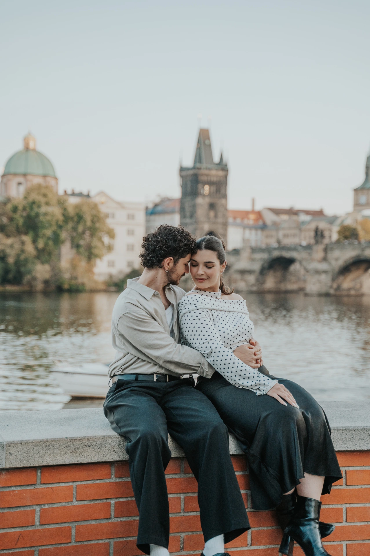 Couple embracing on the low brick wall beside the Vltava during a couple photoshoot in Prague.