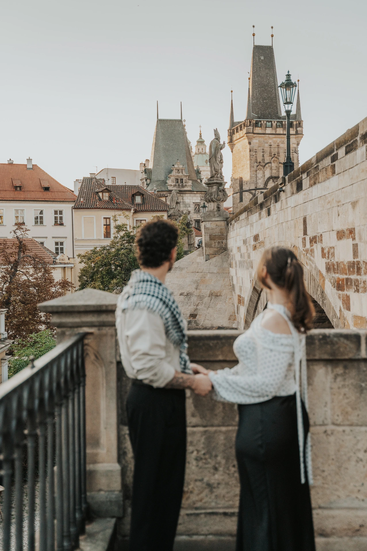 Couple facing each other at the top of the bridge-side steps during a couple photoshoot in Prague.