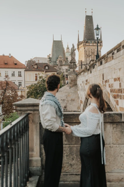Prague couple photoshoot: couple facing each other at the top of the bridge-side steps. Couple facing each other at the top of the bridge-side steps during a couple photoshoot in Prague.