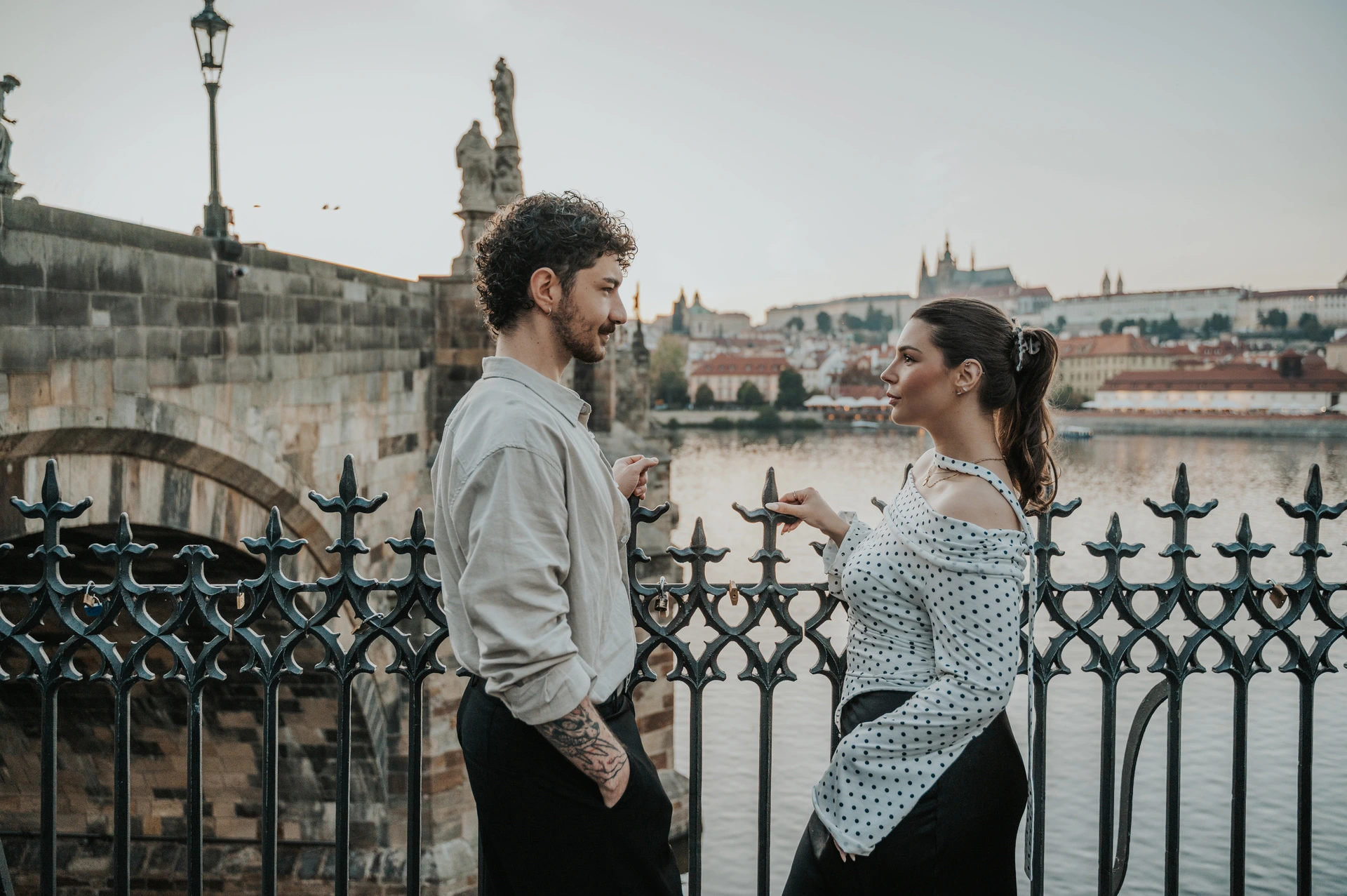 Couple facing one another beside ornate riverside railings during a couple photoshoot in Prague.