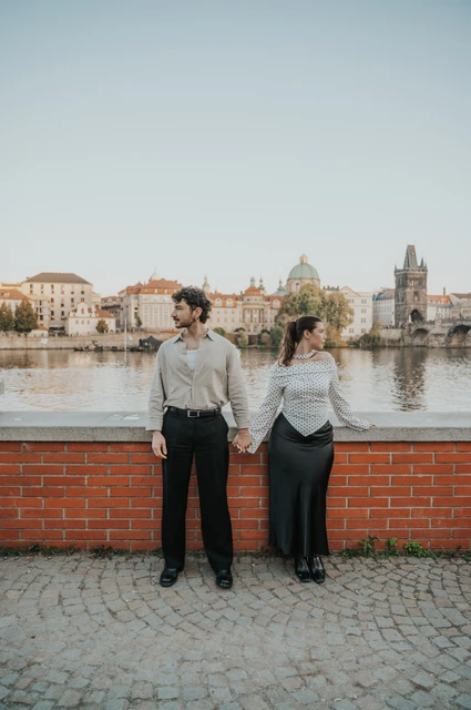 Prague couple photoshoot: couple holding hands against the low brick river wall. Couple holding hands against the low brick river wall during a couple photoshoot in Prague.